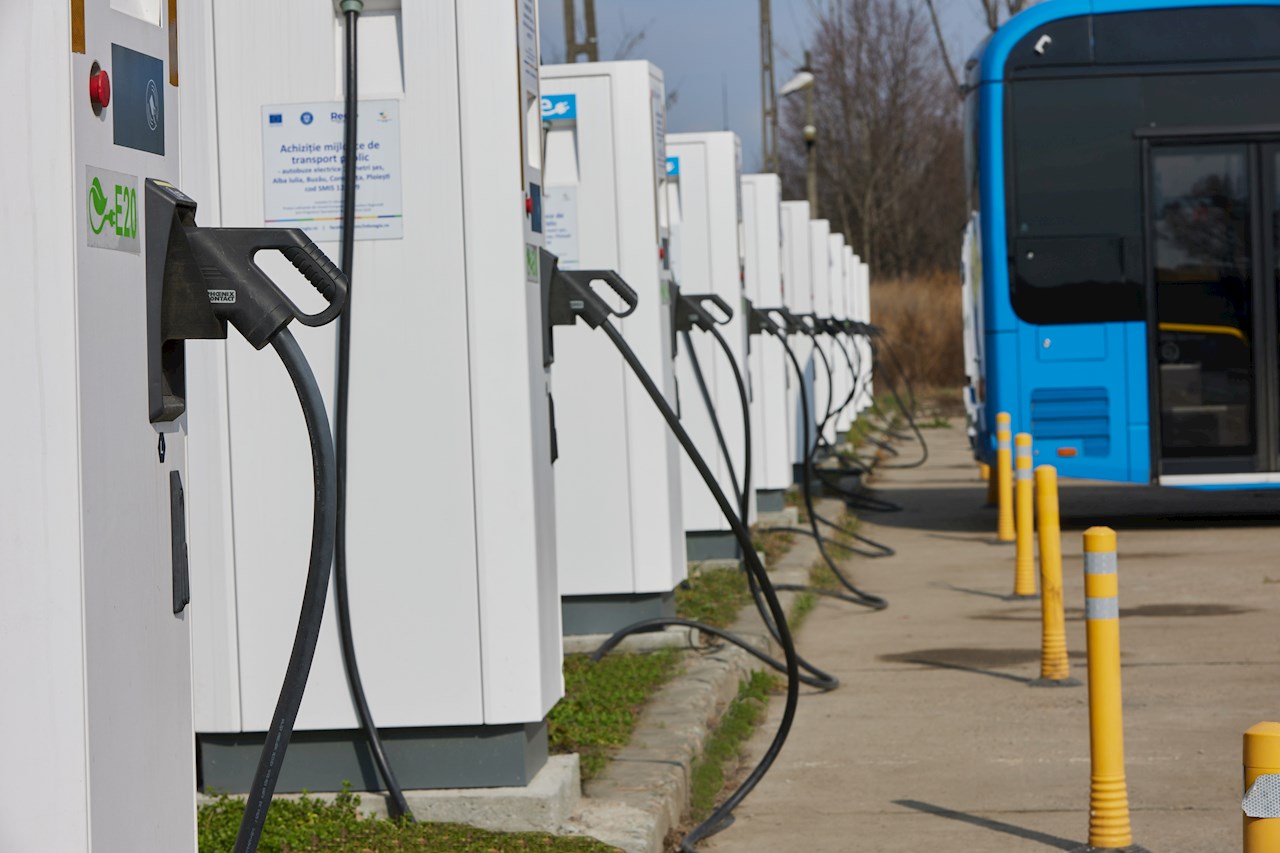 Fila de cargadores ABB blancos con cables de carga junto a un autobús eléctrico azul en el depósito de Constanța, Rumania